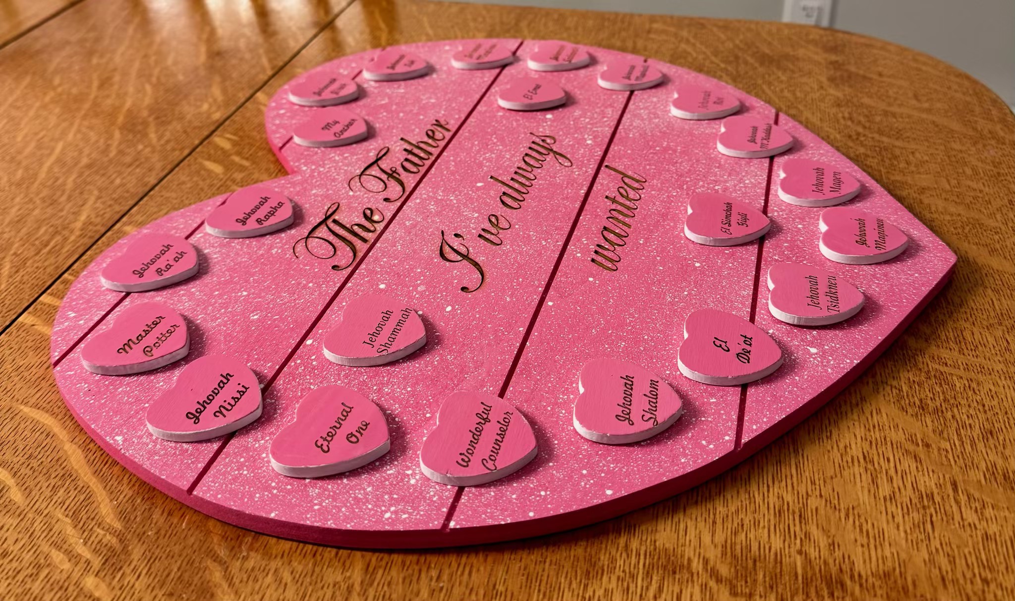 Close-up of the pink glitter heart board showing the engraved heart name tokens of His Names